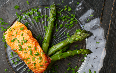 Salmon fillet with asparagus and chives on glass plate dark rough woodの写真素材