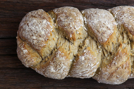 Freshly baked traditional sunflower seed three strand bread plait on dark wooden background