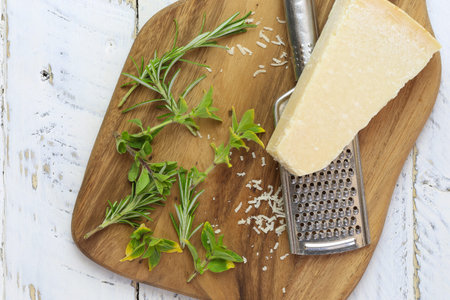Parmesan chess with grater with fresh italian herbs on chopping board and rough white wood background, copy spaceの写真素材