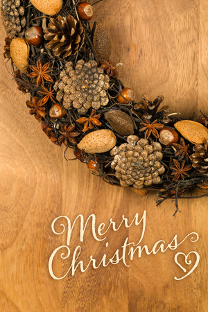 Merry Christmas message, handmade natural wreath decoration pine cones, almonds, anise stars and hazelnuts over wooden background - retro style designの写真素材