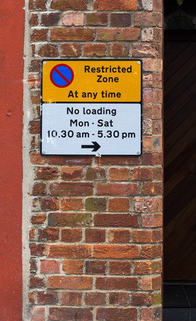 Restricted Zone At Any Time Sign on The Red Brick Wall and No Loading Timesの写真素材
