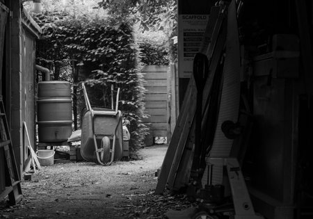 Two metal garden wheelbarrows on the bare ground and rainwater tank near barn
