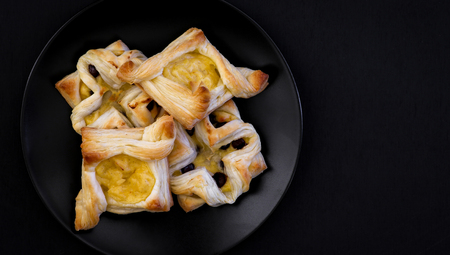 Danish puff pastry flowers and diamonds with vanilla pastry cream and chocolate chips drops on black plate and dark backgroundの写真素材