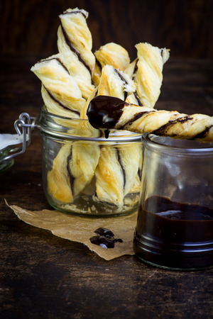 Homemade danish puff pastry twists dipped into melted chocolate in small jar on dark backgroundの写真素材