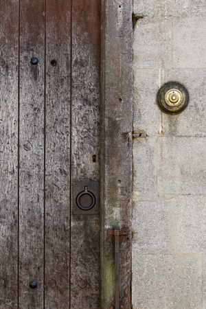 Old rusty metal ring handle on a medieval style aged timber door on stone wall background with brass door bell buttonの写真素材