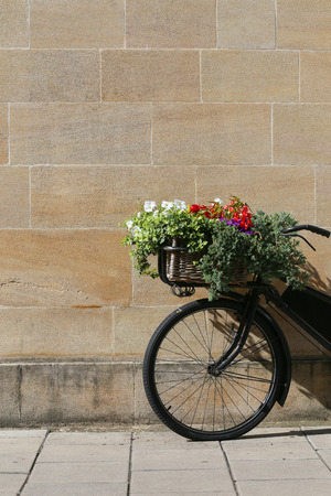 Old vintage black bicycle with wicker basket of flowers leaning against a stone wall in Oxfordの写真素材