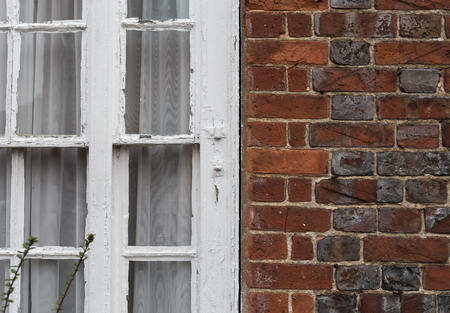 Close up of an old grungy brick wall with white window and chipped paintの写真素材
