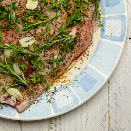 Raw shoulder of lamb meat with olive oil marinade, garlic, thyme, rosemary on plate with blue ornamentの写真素材