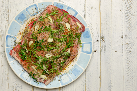 Raw shoulder of lamb meat with olive oil marinade, garlic, thyme, rosemary on plate with blue ornamentの写真素材