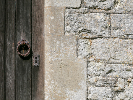 Old weathered wooden door with rusty iron lock and knocker on ancient white stone wallの写真素材