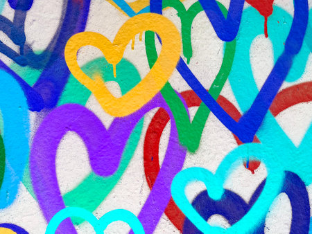 Close-Up of Colorful Graffiti Hearts in Yellow, Purple, Blue, and Green on White Wallの写真素材