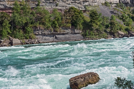 Rock stands against the force of intense white-water rapids in the Niagara river.の写真素材