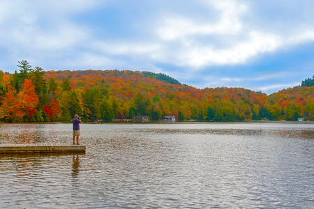 Algonquin, Ontario, Canada - October 2, 2014: Man taking pictures from the deck on the lake. Fall colors in Algonquin park, Ontario, Canada.のeditorial素材