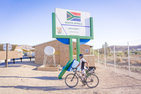 Vioolsdrfif, South Africa - May 3, 2015: Signs at the border between Namibia and Soth Africa. Man on bicycle crossing border.のeditorial素材