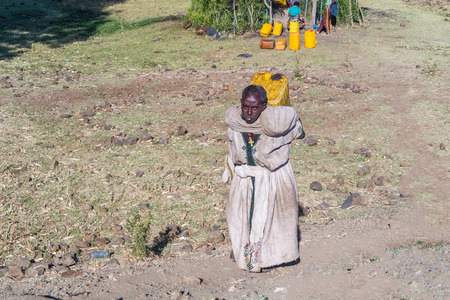 Gondar, Ethiopia - February 10, 2015: Woman in Ethiopia carrying water tank on her back. Picture taken from the road near Gondar in Ethiopia.のeditorial素材