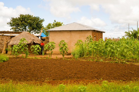 Mbeya, Tanzania - March 20, 2015: Man staying in front of the house, picturesque rural landscape in Tanzania from the road to Mbeya in Tanzaniaのeditorial素材