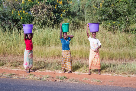 Kasungu, Malawi - March 28, 2015: Three woman carrying buckets on their heads walking by the road near Kasungu in Malawi.のeditorial素材
