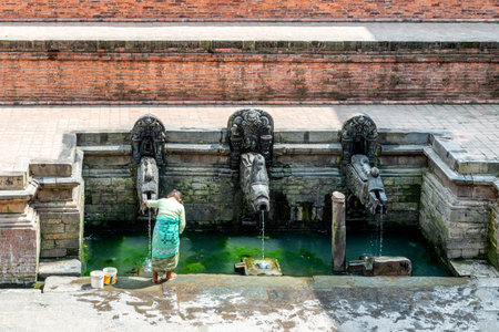 Woman collecting drinking water from the spring on Patan Durbar square, World Heritage Site, Kathmandu valley, Lalitpur, Nepal,のeditorial素材