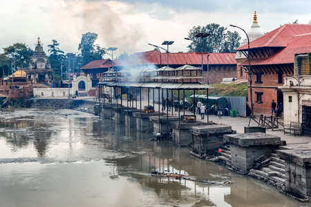 Kathmandu, Nepal - Oct 12, 2018: Friends and family watching cremation of a dead body  at Bagmati River near Pashupatinath Hindu Temple in Kathmandu, Nepal.のeditorial素材