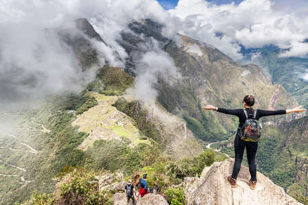 Cusco, Peru â April 6, 2019: Girl standing on the top of Wayna, Huayna Picchu peak at Machu Picchu, The Incas city complex and Machu Picchu mountain peak across at the background.のeditorial素材