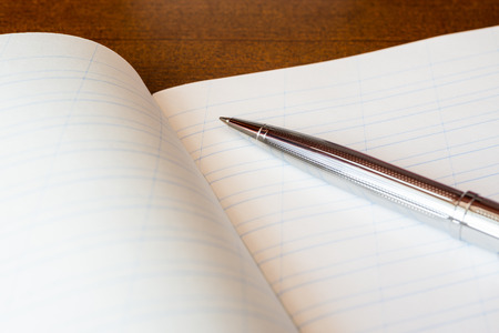 Pen and an exercise book on a wooden tableの写真素材