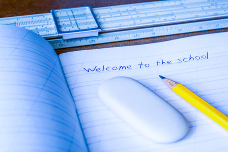 Welcome to the school, an exercise book and pencil with eraser and slide rule on the wooden table....