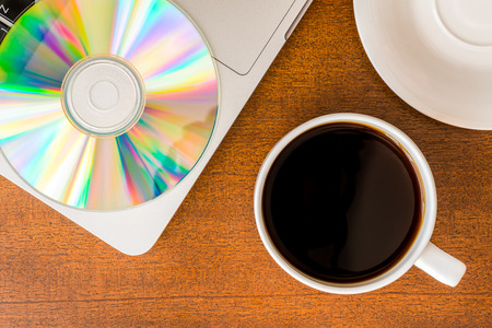Work in the office, coffee cup and a plate with an optical disk with laptop on the wooden tableの写真素材