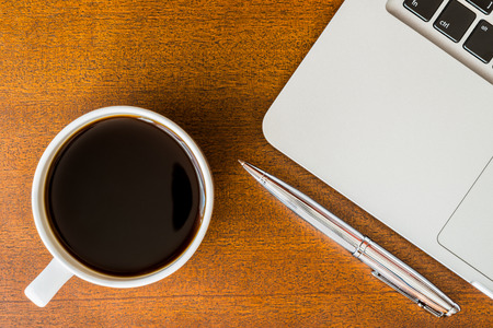 Work in the office, coffee cup with laptop and a pen  on the wooden tableの写真素材