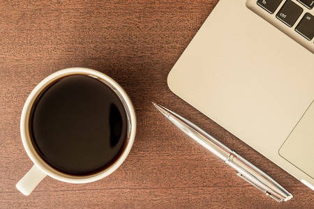 Work in the office, coffee cup with laptop and a pen  on the wooden table. In retro tonesの写真素材
