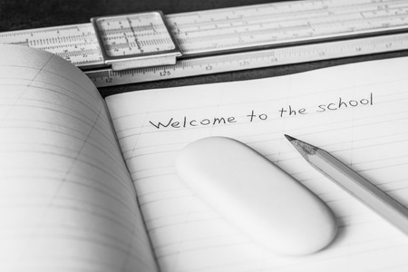 Welcome to the school, an exercise book and pencil with eraser and slide rule on the wooden table. In black and white tonesの写真素材