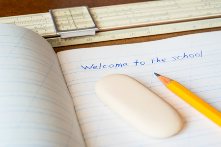 Welcome to the school, an exercise book and pencil with eraser and slide rule on the wooden tableの写真素材