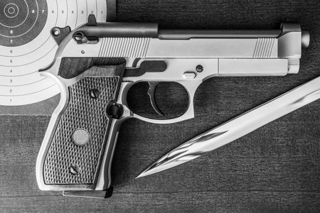 Target shooting, the gun and the target with the knife on the table. Top view, in black and white...