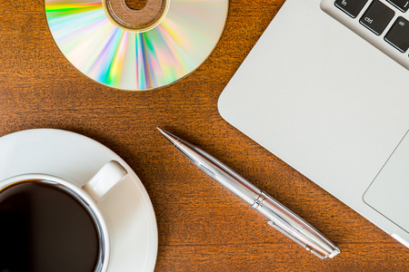 Work in the office, coffee cup and a plate with an optical disk with laptop on the wooden tableの写真素材
