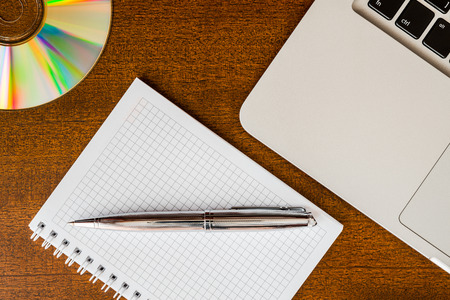 Work in the office, a notebook with a pen and opticak disk with laptop on the wooden tableの写真素材