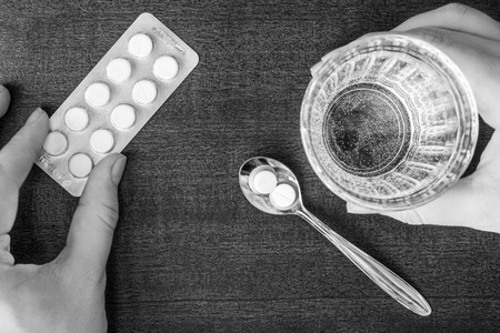 Cure the disease, take the pills in the spoon and drink water. In black and white tonesの写真素材
