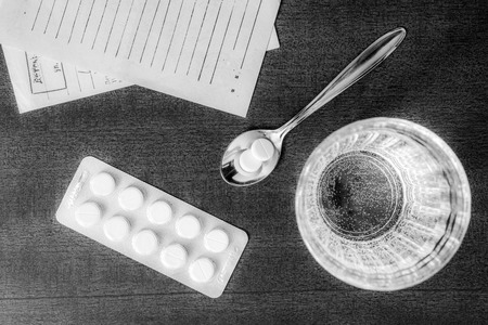 Cure the disease, tablets in the spoon with a glass of water and prescriptions from the doctor on the table. In soft black and white tonesの写真素材