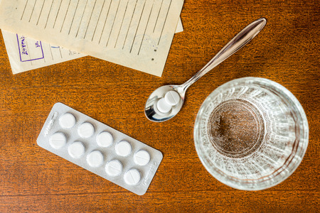 Cure the disease, tablets in the spoon with a glass of water and prescriptions from the doctor on the tableの写真素材