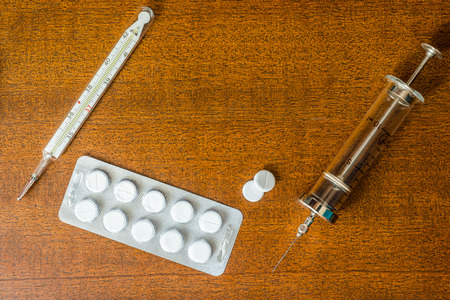 Cure the disease, an injection syringe with a pills and a thermometer on the wooden tableの写真素材
