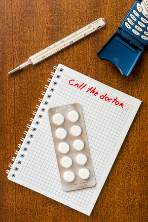 Call the doctor fever heat thermometer with the phone and a pills on the tableの写真素材