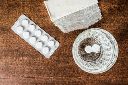 First aid medication dissolved in a glass of water and a bandage. Focus on the glass of water in retro tonesの写真素材