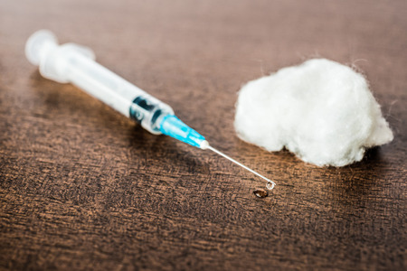 Medicine flows from the syringe and spread out on the table lies next to a cotton swab. Angle view in retro tonesの写真素材