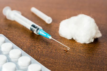 Medicine flows from the syringe and spread out on the table lies next to a cotton swab and a pills. Angle viewの写真素材