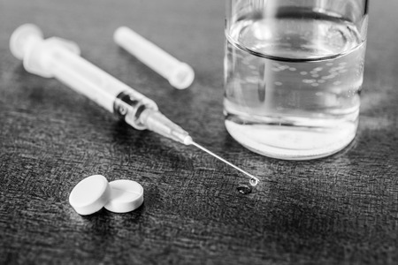 Medicine flows from the syringe and spread out on the table lies next to a two tablets and glass of water. Angle viewの写真素材