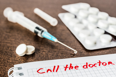 Call the doctor medicine flows from the syringe and spread out on the table lies next to the pills. Angle view focus on the signの写真素材