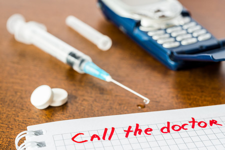 Call the doctor medicine flows from the syringe and spread out on the table lies next to the phone. Angle view focus on the signの写真素材