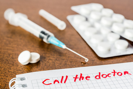Call the doctor, medicine flows from the syringe and spread out on the table, lies next to the pills. Angle view, focus on the signの写真素材