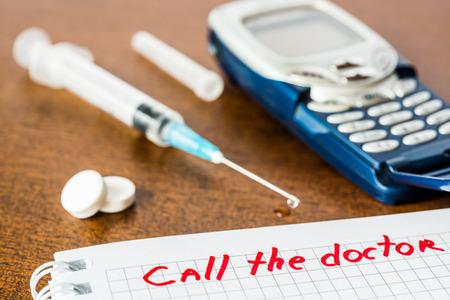 Call the doctor, medicine flows from the syringe and spread out on the table, lies next to the phone. Angle view, focus on the signの写真素材
