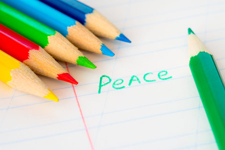 Word peace written in a notebook with colored pencils, green pencil lying on the notebookの写真素材