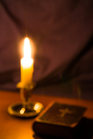 Old bible and candle on a wooden table. Image is out of focusの写真素材