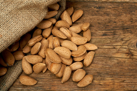 Almond nuts in a burlap bag on a wooden background.の写真素材